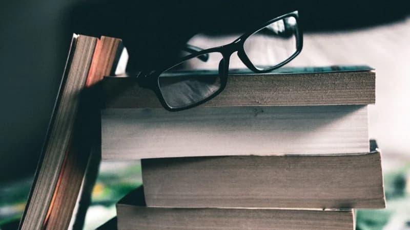 Stacked study books with reading spectacles